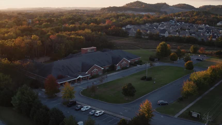 A large building is shown surrounded by fall trees at sunset