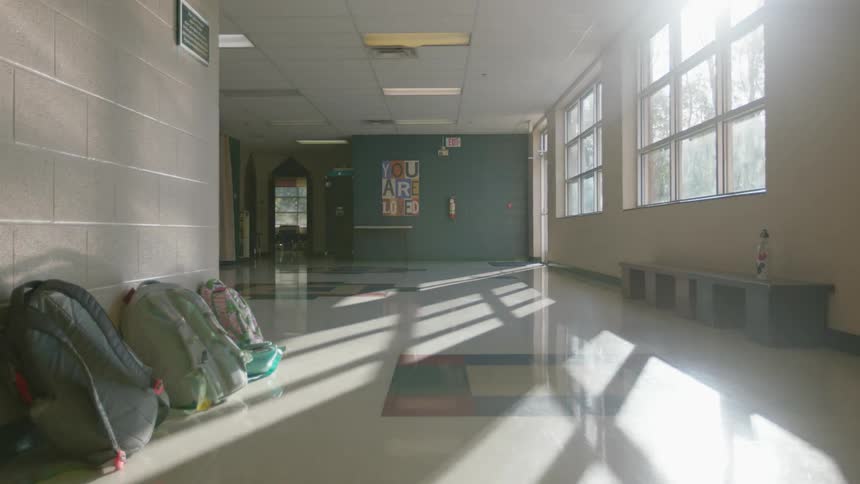 Backpacks sit stacked against a schoolhouse wall
