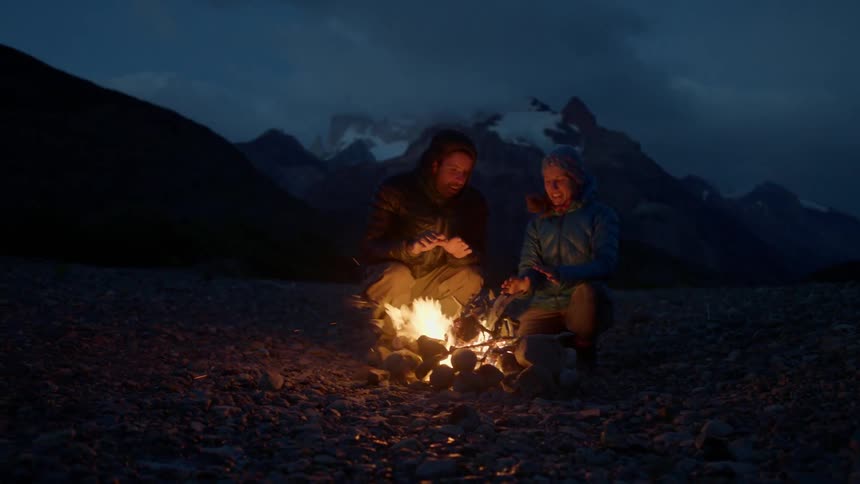 A man and a woman talking near a campfire