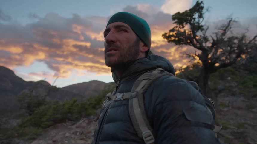 A hiker stands in the mountains at sunset