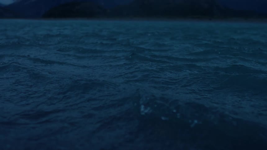 Small ripples flow in the water in front of snowy mountains