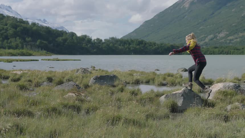 A woman leaps onto a rock next to a mountain lake