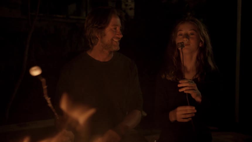 A man and a woman are roasting marshmallows on a stick next to a fire