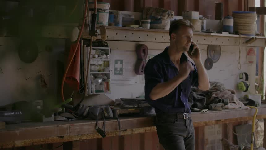 A man talks on a phone while standing in a workshop