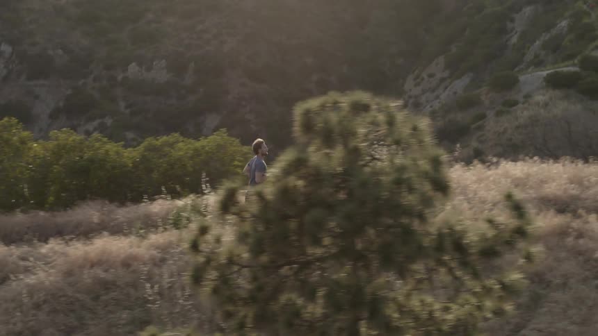 Man jogs over weedy hilly land