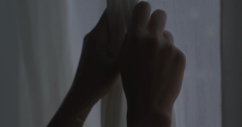 Two hands open curtains on a window