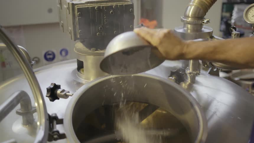 A worker pours a liquid into a large metal vat