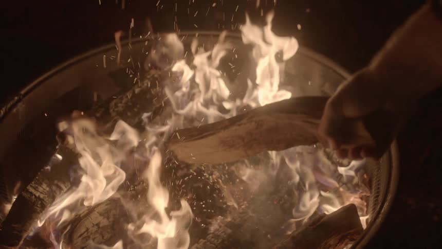 A person adding a log to a fire