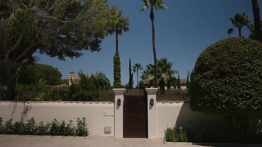 Trees blowing in the wind around a building and gate on a clear sunny day