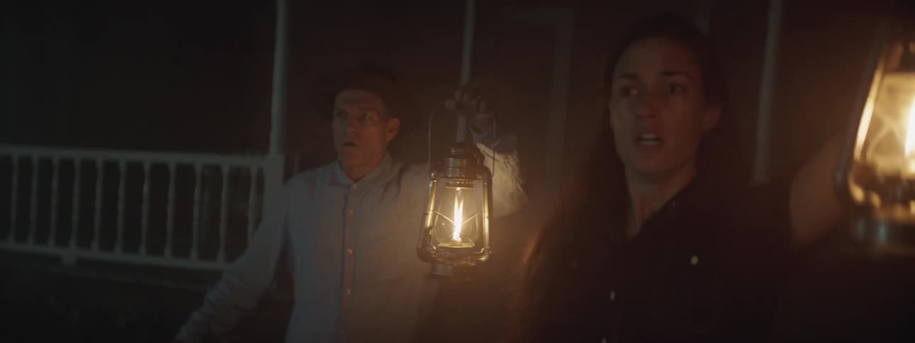 Woman and man hold lanterns running out of a house at night shouting