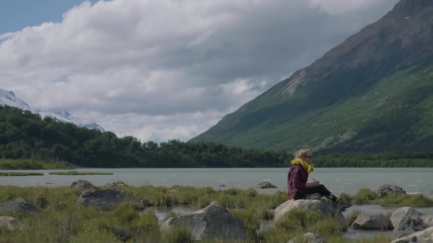 A woman sits on a rock in a lake