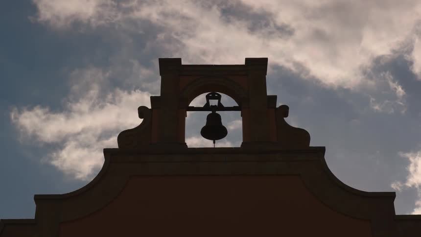 Clouds float over a building and large bell