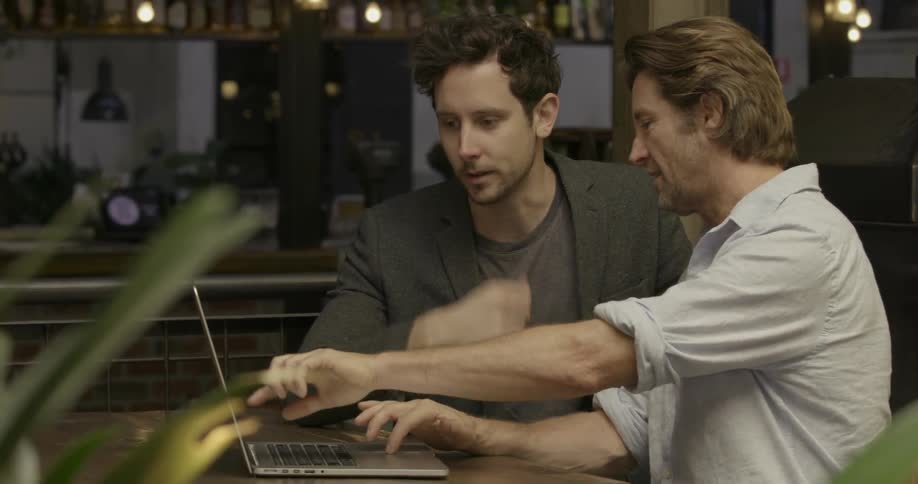 Two men are sitting at a table using a laptop