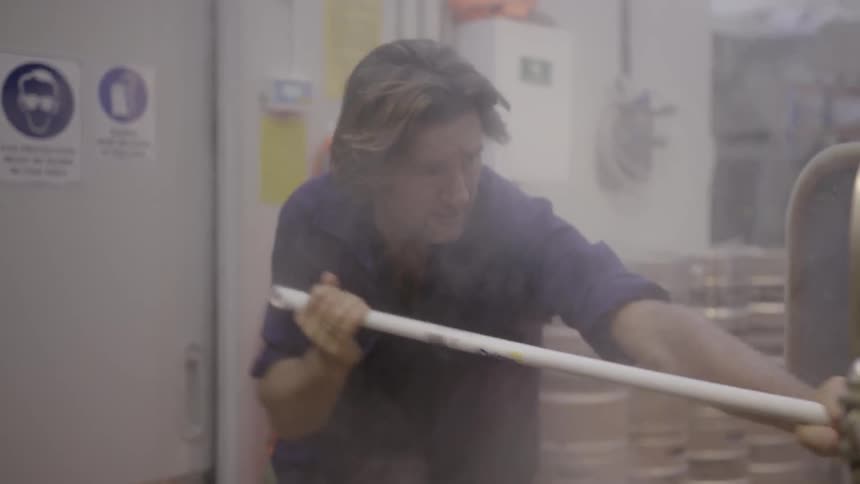 Man scooping dark sandy material into a bin