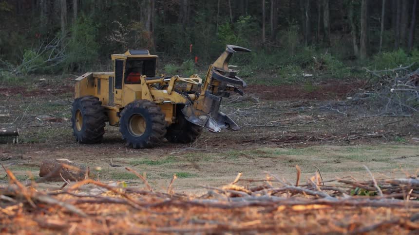 Tractor rolls over bumpy land with woods in the background