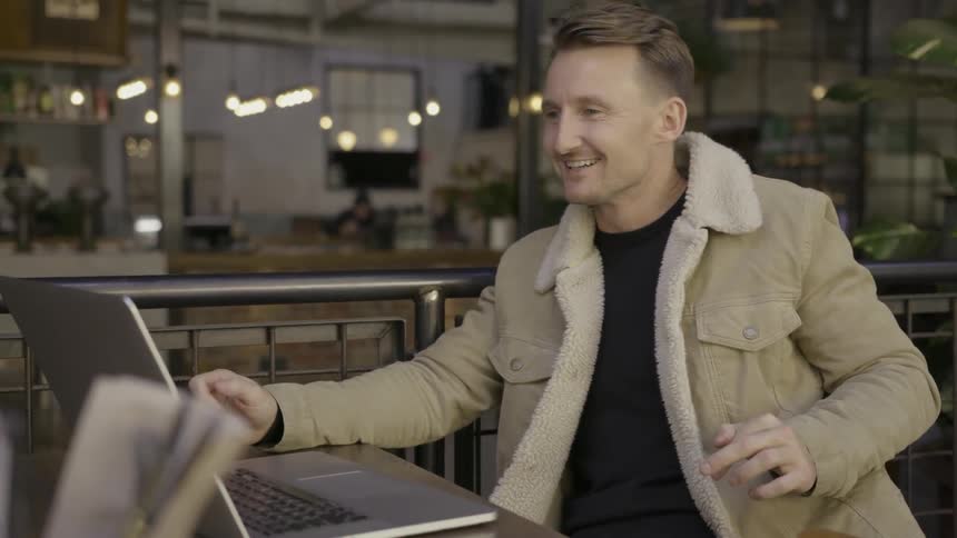 A man with a laptop in front of him is talking to someone