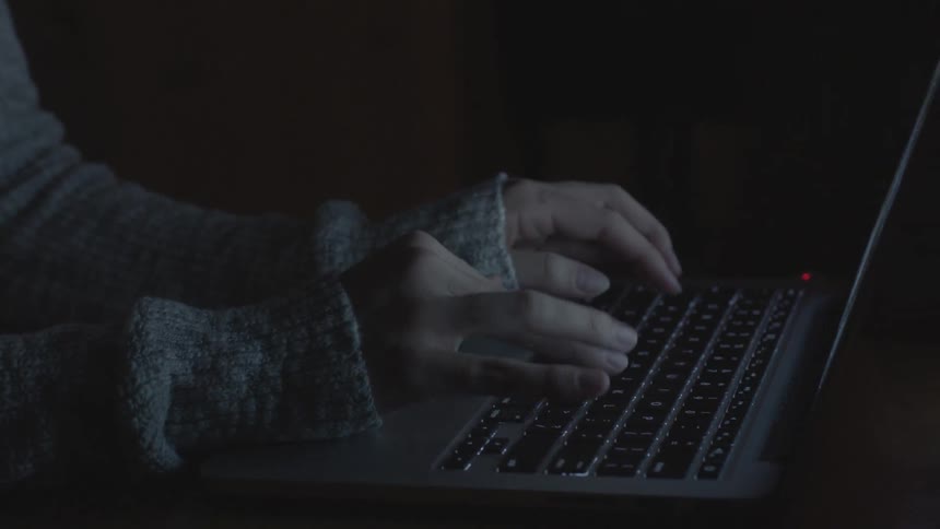 Woman typing on a laptop in a dark room
