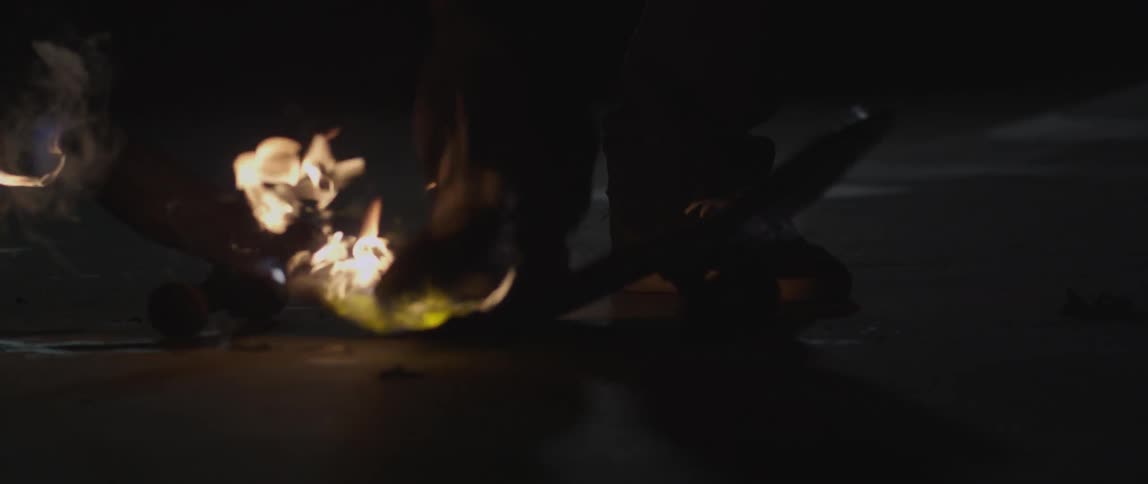 A man stomps on a skateboard that has been lit on fire