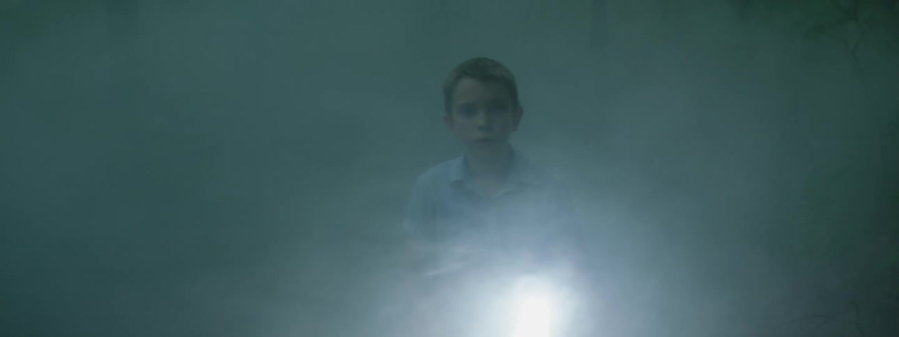 A child walks out of the smoke with a flashlight