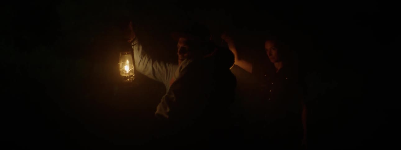 A man holding a child and a woman are walking in the dark with lamps