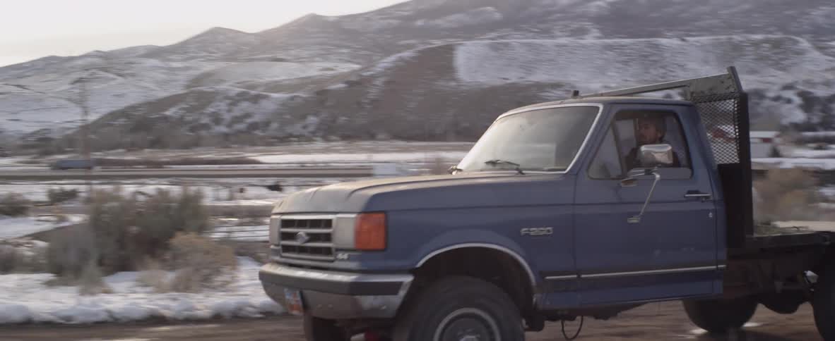 A man drives a flatbed truck on a dirt road