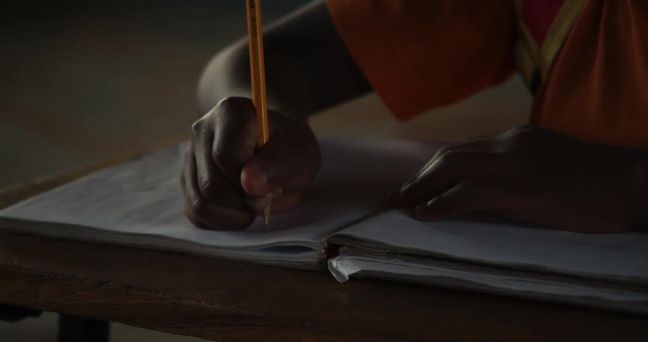 Someone is writing in a book while sitting at a desk