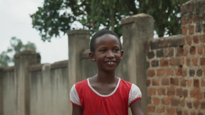 Young child in a red shirt walks near a brick wall