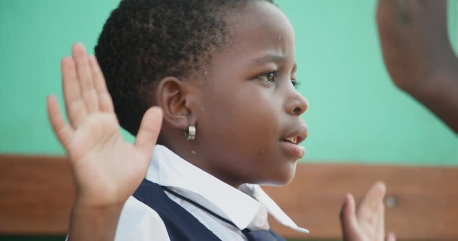 A young child claps her hands against the palms of another person