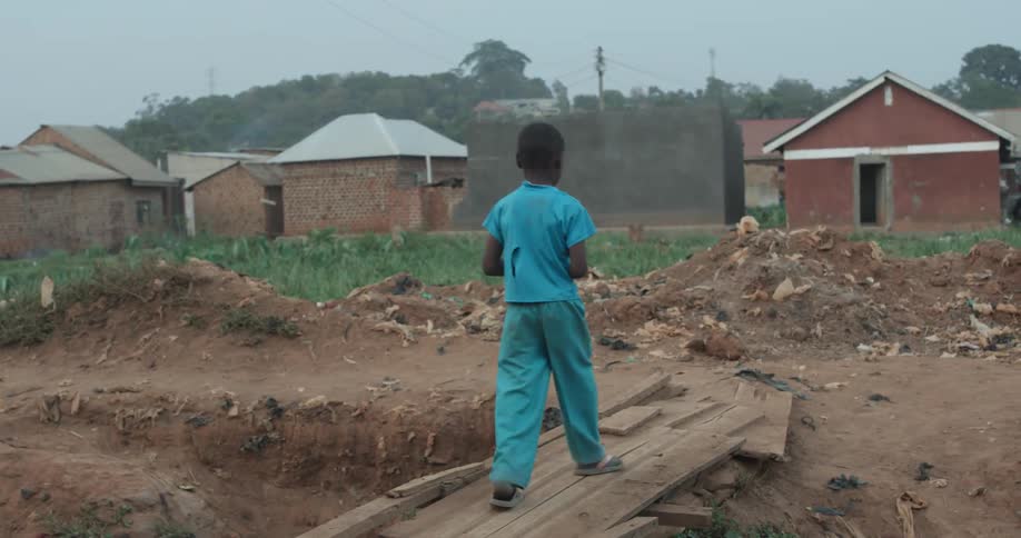 Child walks across a wood plank towards small houses