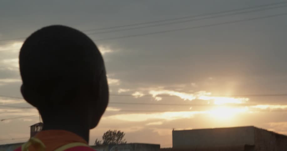 A boy wearing a backpack walks outside at sunset