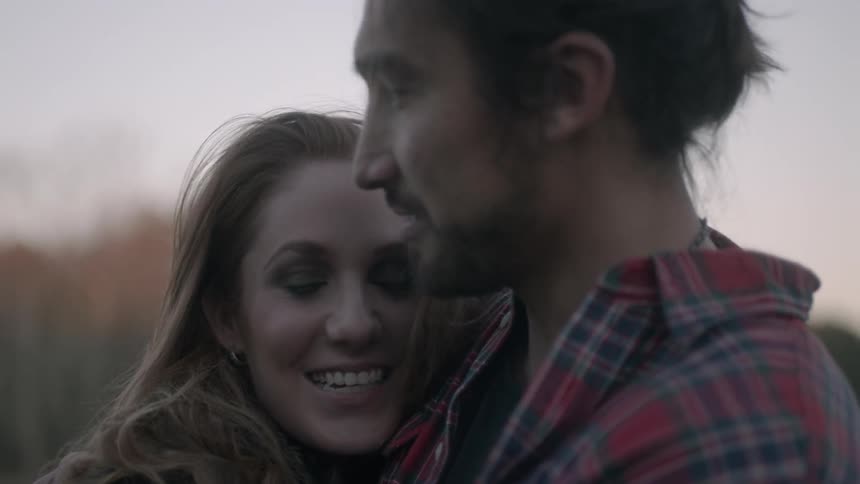 A man and woman hug and laugh while near a pond