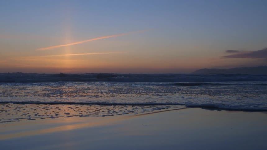 Waves roll onto a beach at sunset
