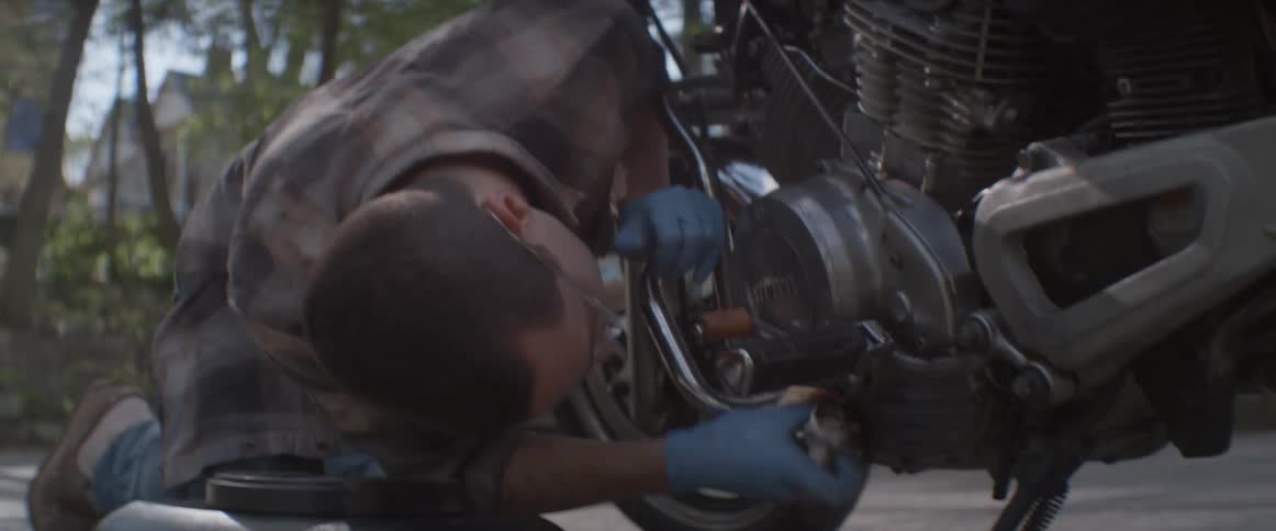 Man cleaning parts of motorcycle outside during the day