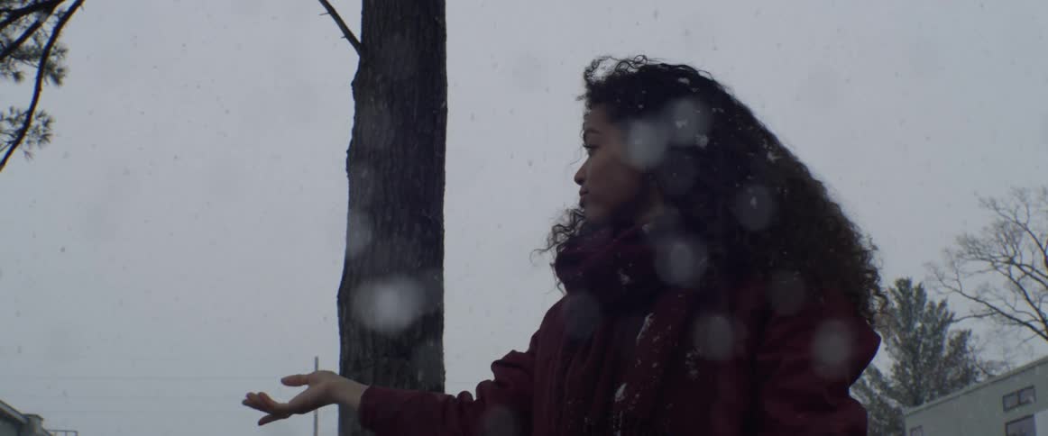 A woman holds her hands up to catch snowflakes as they fall