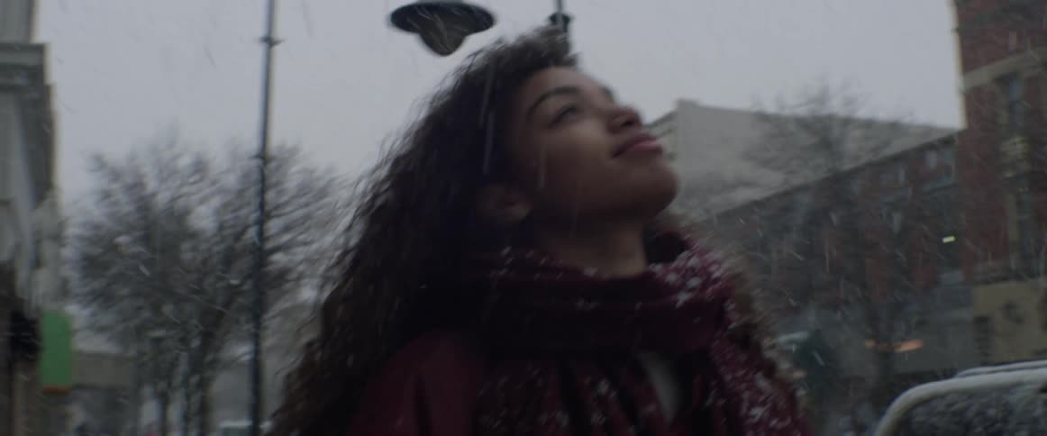 A woman smiles and looks up at the sky as snow falls