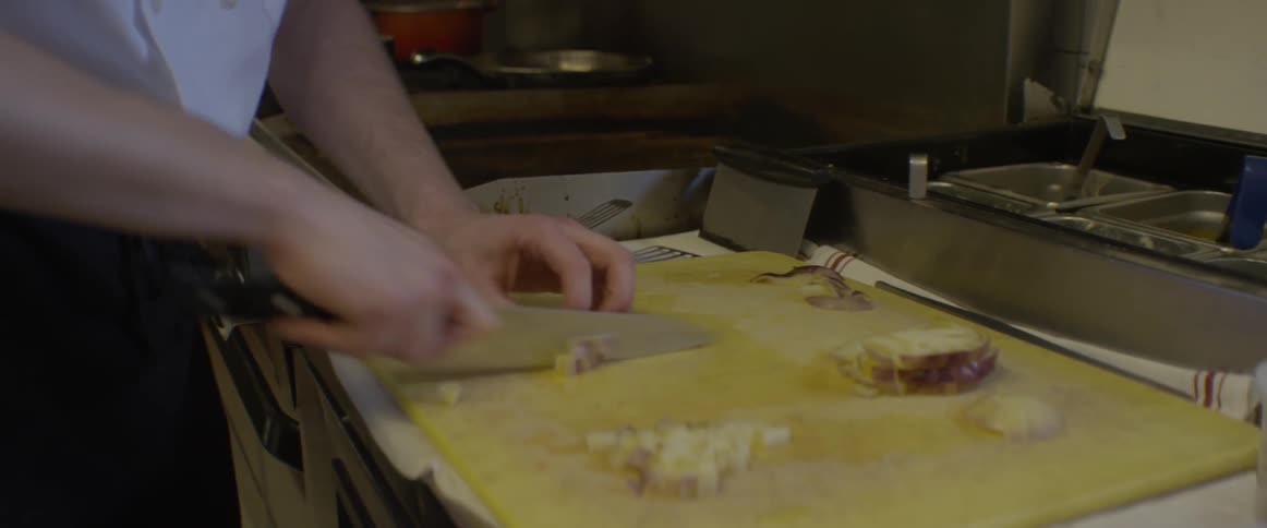 A chef is dicing food on countertop in a kitchen