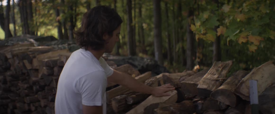 Man carrying logs puts them in a large stack