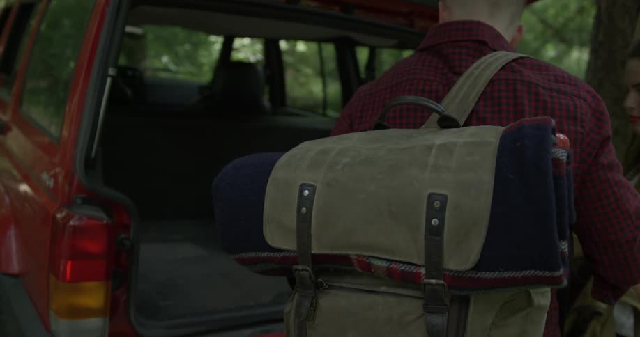 A man and a woman are at the back of an suv getting stuff out of the trunk