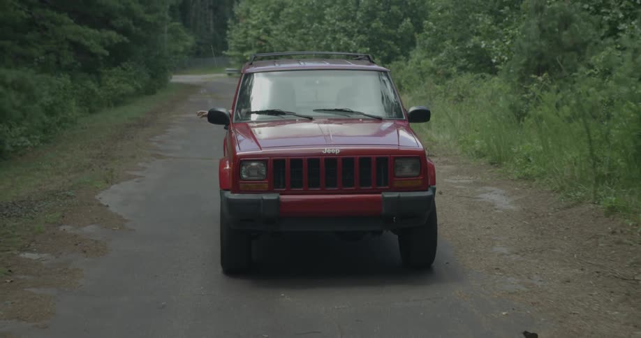 Red jeep drives down a narrow path in the country
