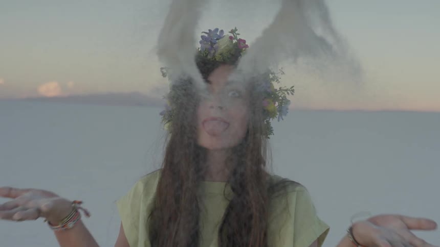 Woman wearing flower wreath on head sticking out tongue and tossing sand
