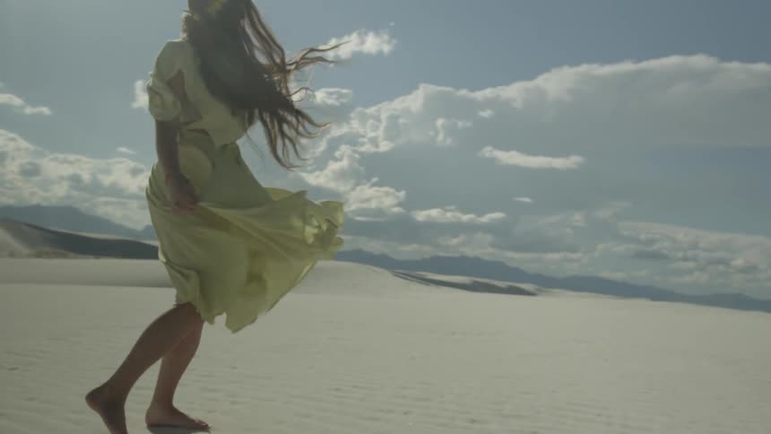 A woman walks in a desert on a windy day