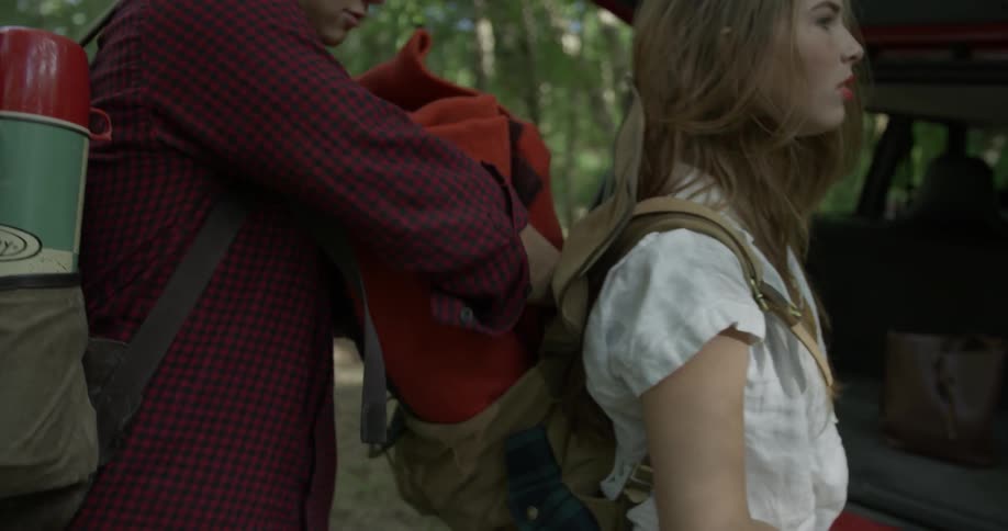 A man loads some blankets in a woman's backpack