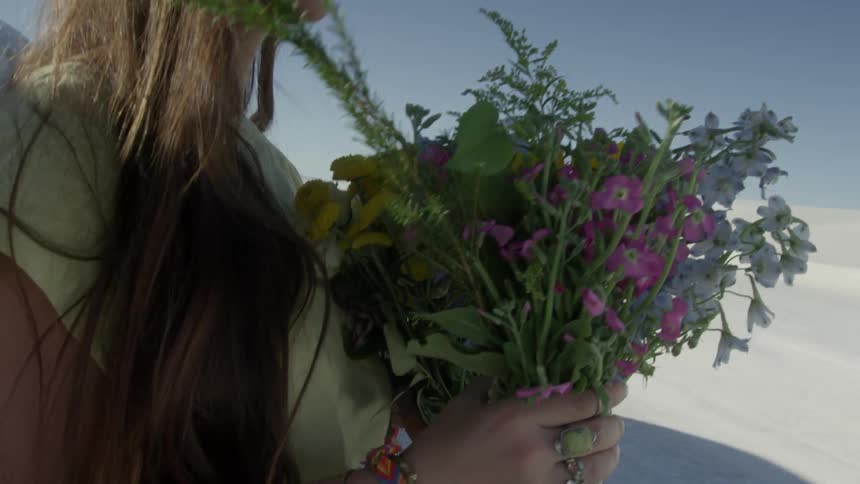 A woman carries a bouquet of flowers into the desert