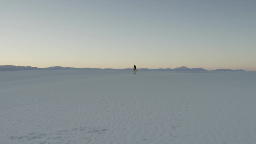 A woman with long hair wearing a dress walks on sand