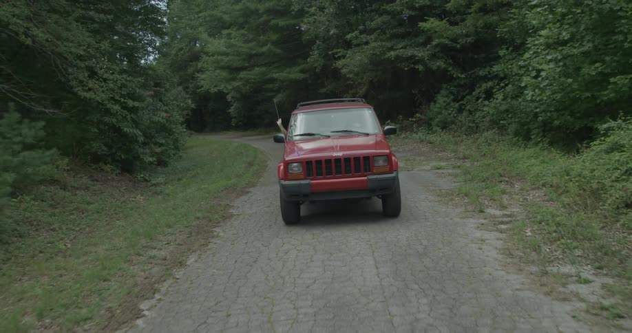 A red truck drives down a small road in the forest