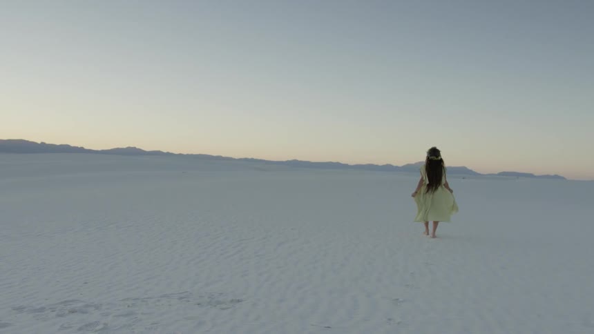 A woman flounces her skirt as she walks over white sands