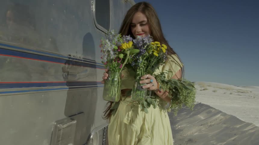 A woman carrying vases of flowers walks by a van