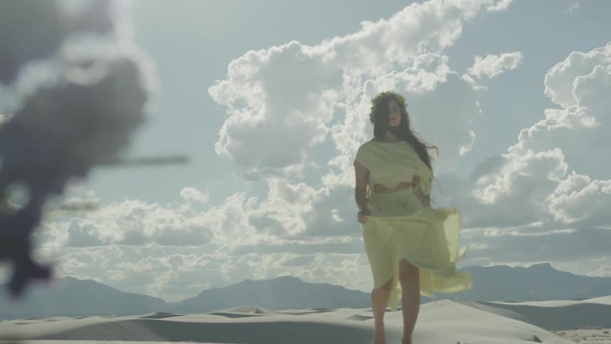 A woman wearing a yellow dress walks in the sand