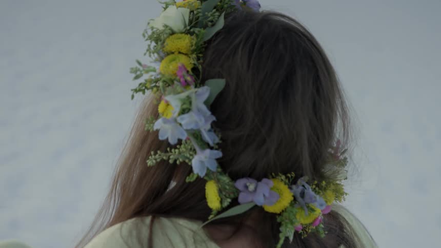 A woman wears a flower wreath on her head in a desert at sunset