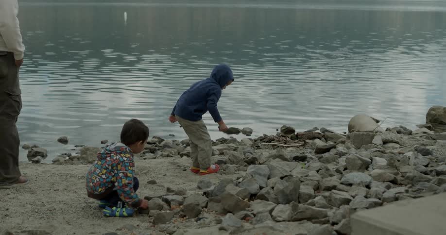 Man and two children stand at the edge of water throwing rocks in